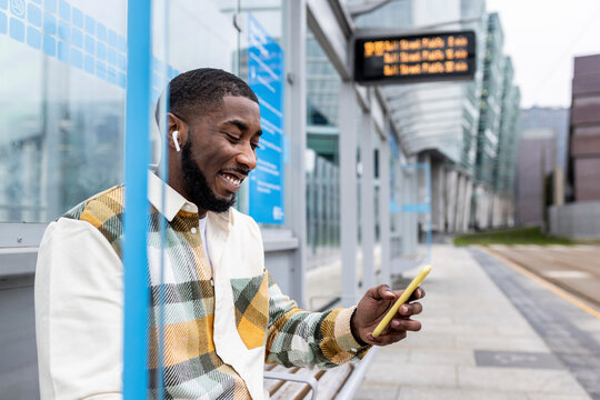 Happy man surfing net through mobile phone sitting t tram station