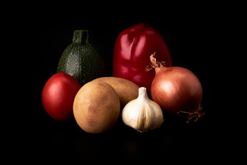 Potatoes, onion, red bell pepper, tomato, zucchini and garlic on a black background. Healthy and vegetarian food