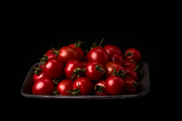 Fresh red tomatoes on a black tray on a black background. Vegan and vegetarian food