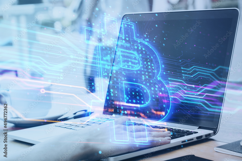 Poster close up of hands using laptop computer keyboard with creative blue bitcoin hologram on blurry offic