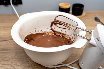 A standing hand mixer with a whisk next to the bowl, with raw dough, the dough is in a thick liquid brown state.