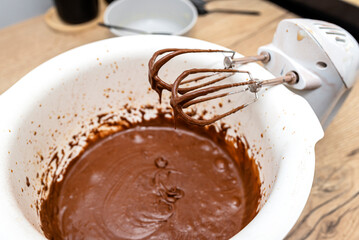 A standing hand mixer with a whisk next to the bowl, with raw dough, the dough is in a thick liquid brown state.