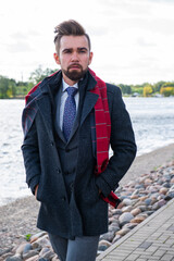 A man in a coat and business suit poses in Latvia
