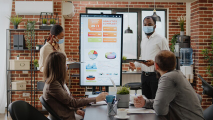African american workmates presenting marketing strategy to colleagues, using tablet and monitor in startup office. People planning business growth and development during covid 19 pandemic.
