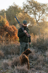 Hunter resting his gun on his shoulder while looking at his dog
