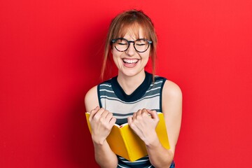 Redhead young woman reading a book wearing glasses smiling and laughing hard out loud because funny...
