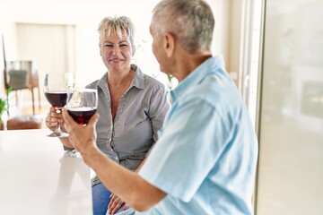 Senior caucasian couple smiling happy toasting with wine at the kitchen.