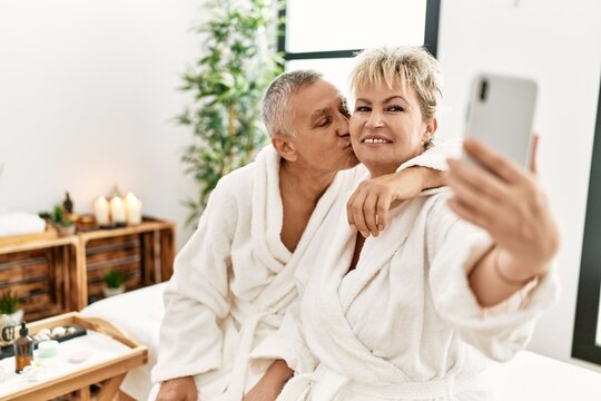 Senior caucasian couple smiling happy making selfie by the smartphone sitting on massage table at beauty center.