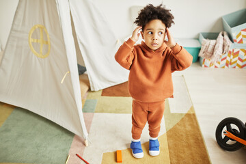 Full length portrait of cute African American toddler looking surprised and scared while playing at...