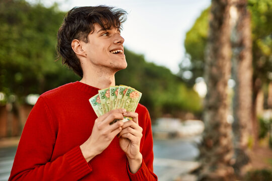 Young hispanic man smiling happy holding argentinian pesos banknotes at the city
