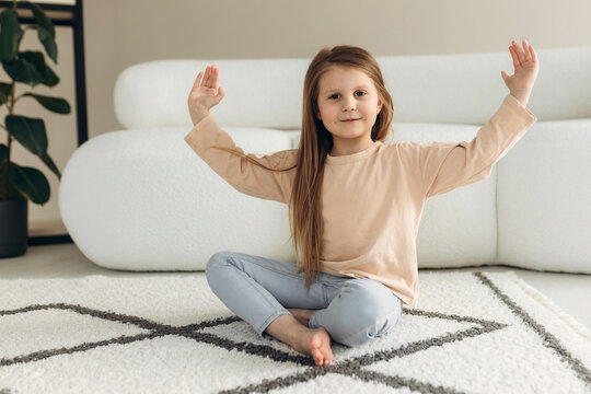 Portrait of a little cute girl. She is sitting on the floor near the sofa. The girl looks at the camera