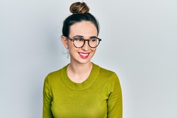 Young hispanic girl wearing casual clothes and glasses looking away to side with smile on face, natural expression. laughing confident.