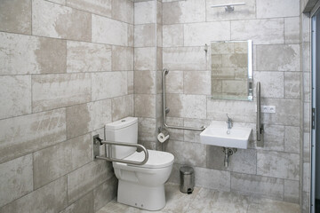 modern bathroom interior with white toilet, handicapped rails, white sink and mirror
