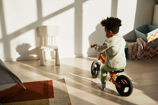 Minimal back view portrait of African American little boy riding balance bike at home in sunlight, copy space
