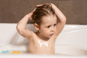 Cute three year old boy taking a bath with foam.