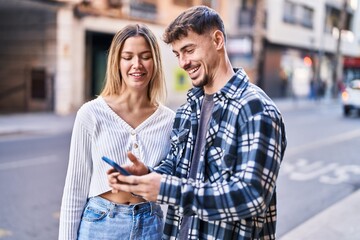 Young man and woman couple smiling confident using smartphone at street