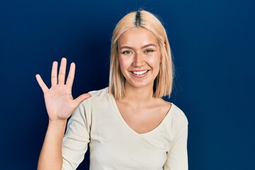 Beautiful blonde woman wearing casual sweater showing and pointing up with fingers number five while smiling confident and happy.