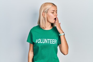 Beautiful blonde woman wearing volunteer t shirt bored yawning tired covering mouth with hand....