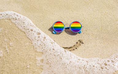 Fototapeta na wymiar Sunglasses with LGBT flag on a sandy beach. Summer travel concept