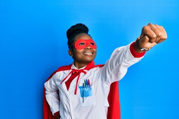African american doctor woman wearing medical coat and super hero mask and coat doing power gesture