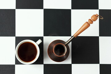 A cup of coffee and a coffee pot on a chessboard.