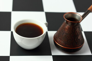 A cup of coffee and a coffee pot on a chessboard.