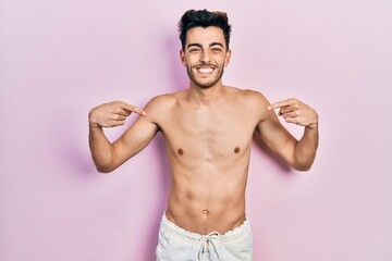 Fototapeta premium Young hispanic man wearing swimwear shirtless looking confident with smile on face, pointing oneself with fingers proud and happy.