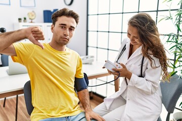 Young doctor woman checking blood pressure on patient with angry face, negative sign showing dislike with thumbs down, rejection concept
