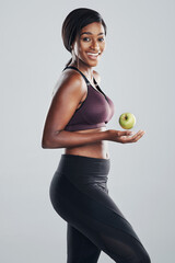 Shes getting ready to hit the gym. Studio portrait of an attractive and fit young woman posing with an apple in her hand against a grey background.
