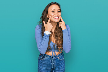 Young hispanic girl wearing casual clothes smiling with open mouth, fingers pointing and forcing cheerful smile