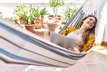 Young hispanic girl using laptop lying on hammock at the terrace.