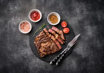 Gordijnen Medium rare Ribeye steak or beef steak on the black tray with tomatoes. Top view, flat lay. © FoodAndPhoto