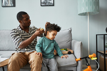 Portrait of young father brushing hair of cute little boy while taking care of son indoors, copy space