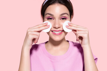 Smiling modern  girl cleaning face skin, removing makeup, using cotton pads and cleansing product....