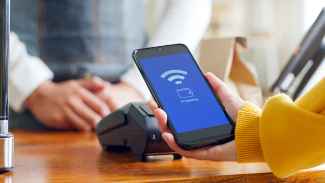 Customer using smartphone for NFC payment at cafe restaurant, cashless, contactless technology and money transfer concept