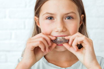 Attractive little girl stands on white background. Dental simulator for teeth alignment . The child has mouth guards on his teeth