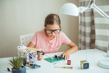 Cute girl constructs metal robot and program it. The boards and microcontrollers are on the table. STEM education inscription. Programming. Mathematics. The science. Technologie. DIY