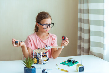 Smart little girl learn at home in coding robot cars and electronic board cables in STEM,...