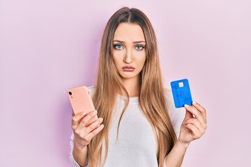 Young blonde girl holding smartphone and credit card depressed and worry for distress, crying angry and afraid. sad expression.