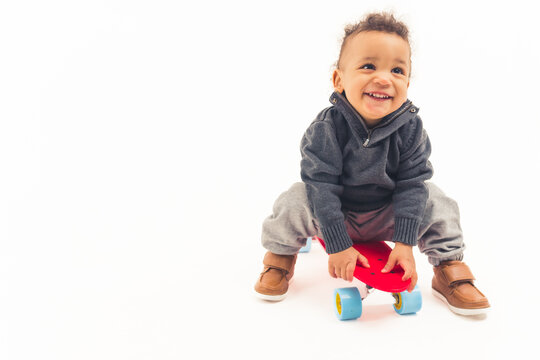 Cute joyful interracial toddler in the studio playing with red mini skateboard and laughing over white background. High quality photo
