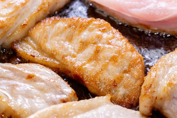 Pieces of fried pork meat in oil. Drops of oil in a frying pan. Selective focus