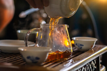 A hand that pours Chinese tea from a glass teapot into a small cup. Selective focus