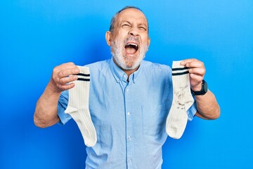 Handsome senior man with beard holding clean andy dirty socks angry and mad screaming frustrated...