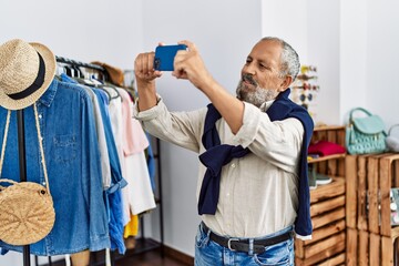 Senior grey-haired man making selfie by the smartphone at clothing store
