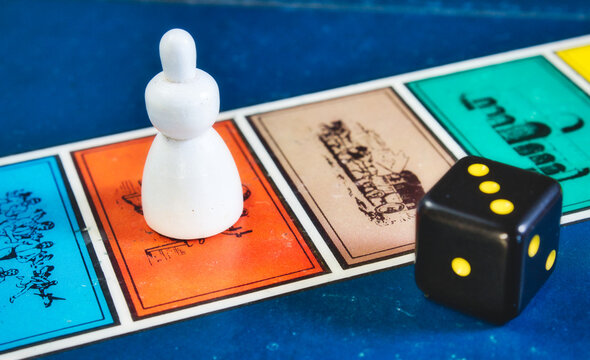 Close-up Of Board Game Squares With Player Piece And Black Die With Yellow Dots