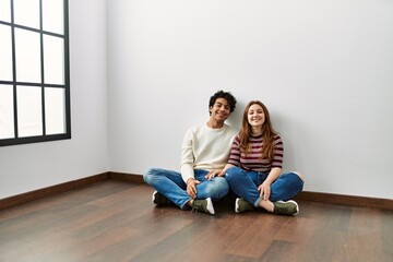 Young hispanic couple smiling happy sitting on the floor at empty new home.