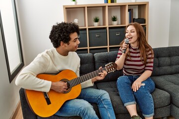 Young couple playing classical guitar and singing using microphone at home.