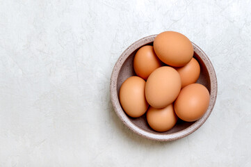 Brown raw eggs in a bowl on a light background. Top view with copy space.