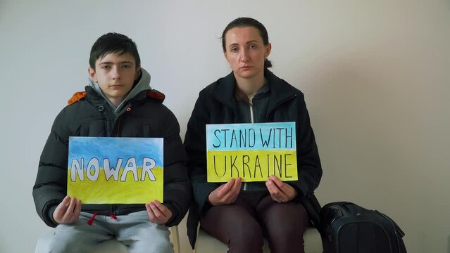 Refugee mother and son holding motivational packard with text No war and Stand with Ukraine against armored conflict. Crisis, peace, stop aggression in whole world