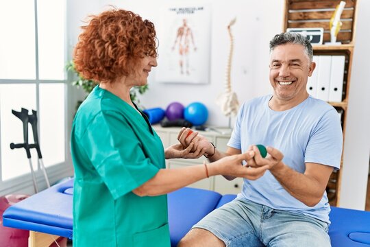 Middle age man and woman wearing physiotherapy uniform having rehab session using balls at physiotherapy clinic